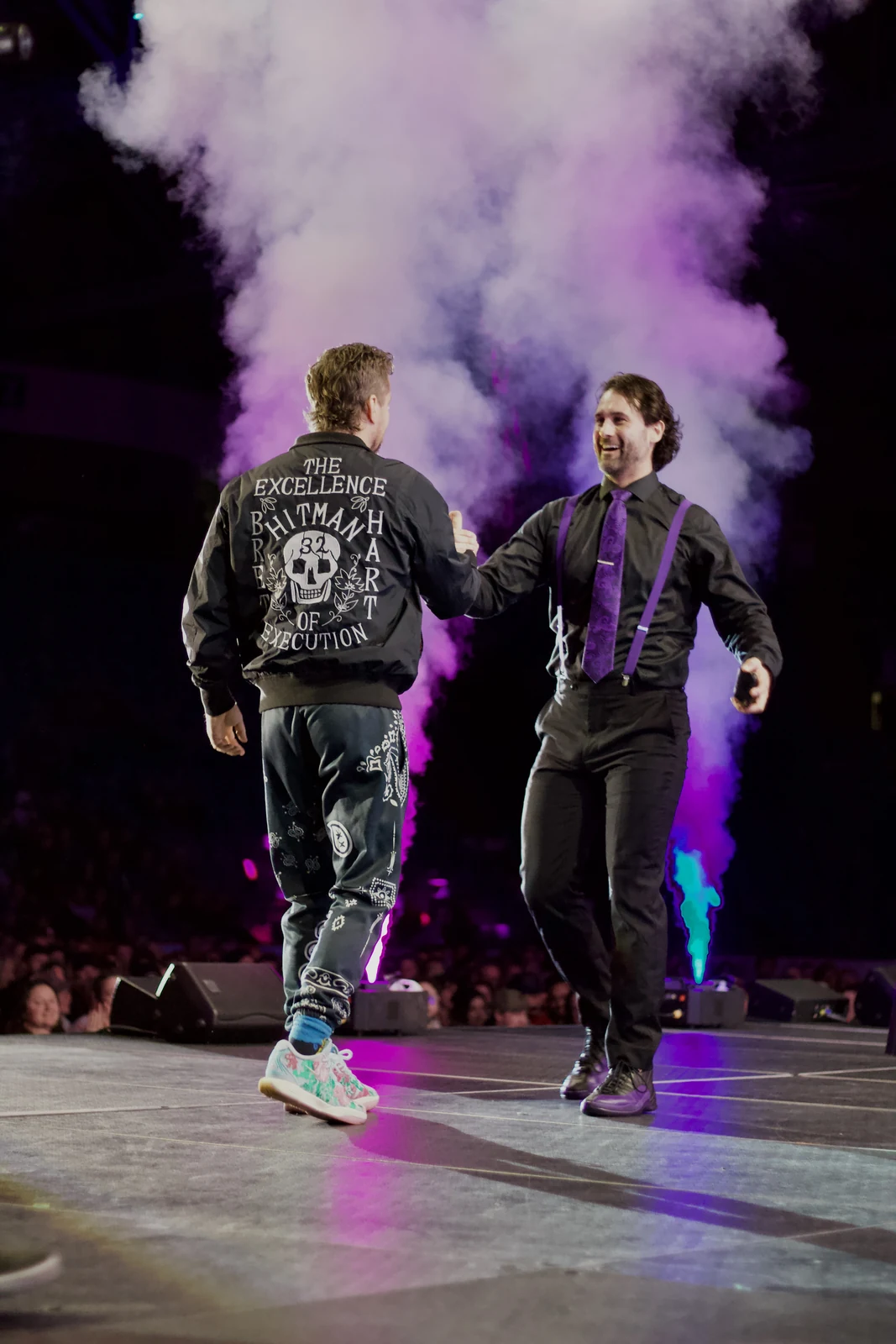 Two performers sharing a moment on stage amid colourful smoke