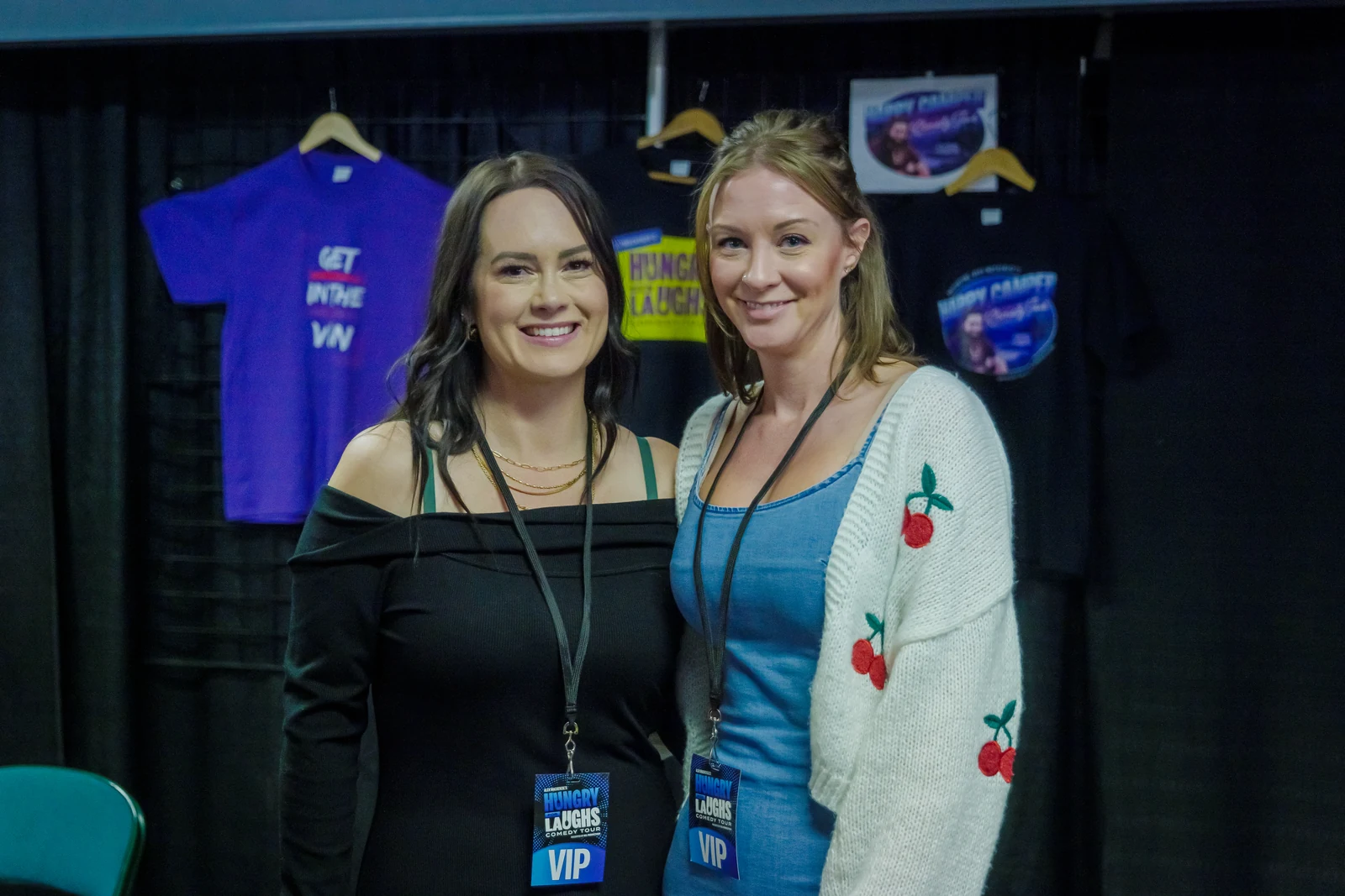 Two guests smiling beside the tour merchandise